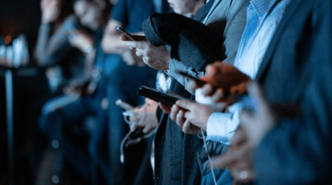 Photo of a group of people focussed in on them holding their phones. 