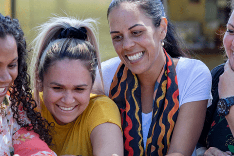 A photo of five women looking and smiling at a shared item that is not in the frame. 